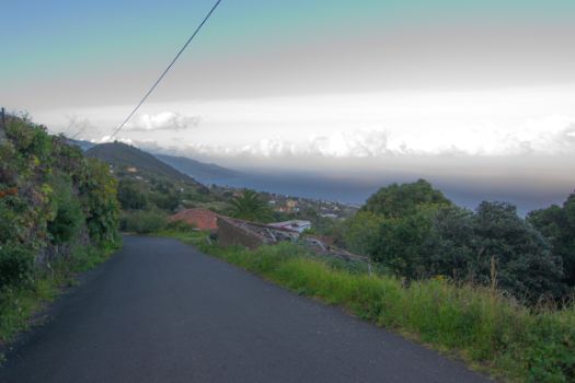 El camino desciende por una pista asfaltada con las vistas del océano Atlántico y la montaña de La Breña