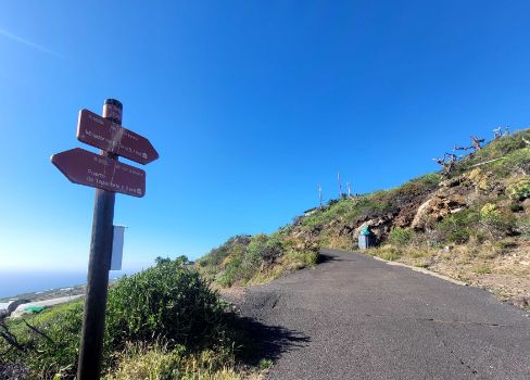 Señal de Caminos Naturales y vegetación costera en tramo de asfalto previo al Mirador del Time.